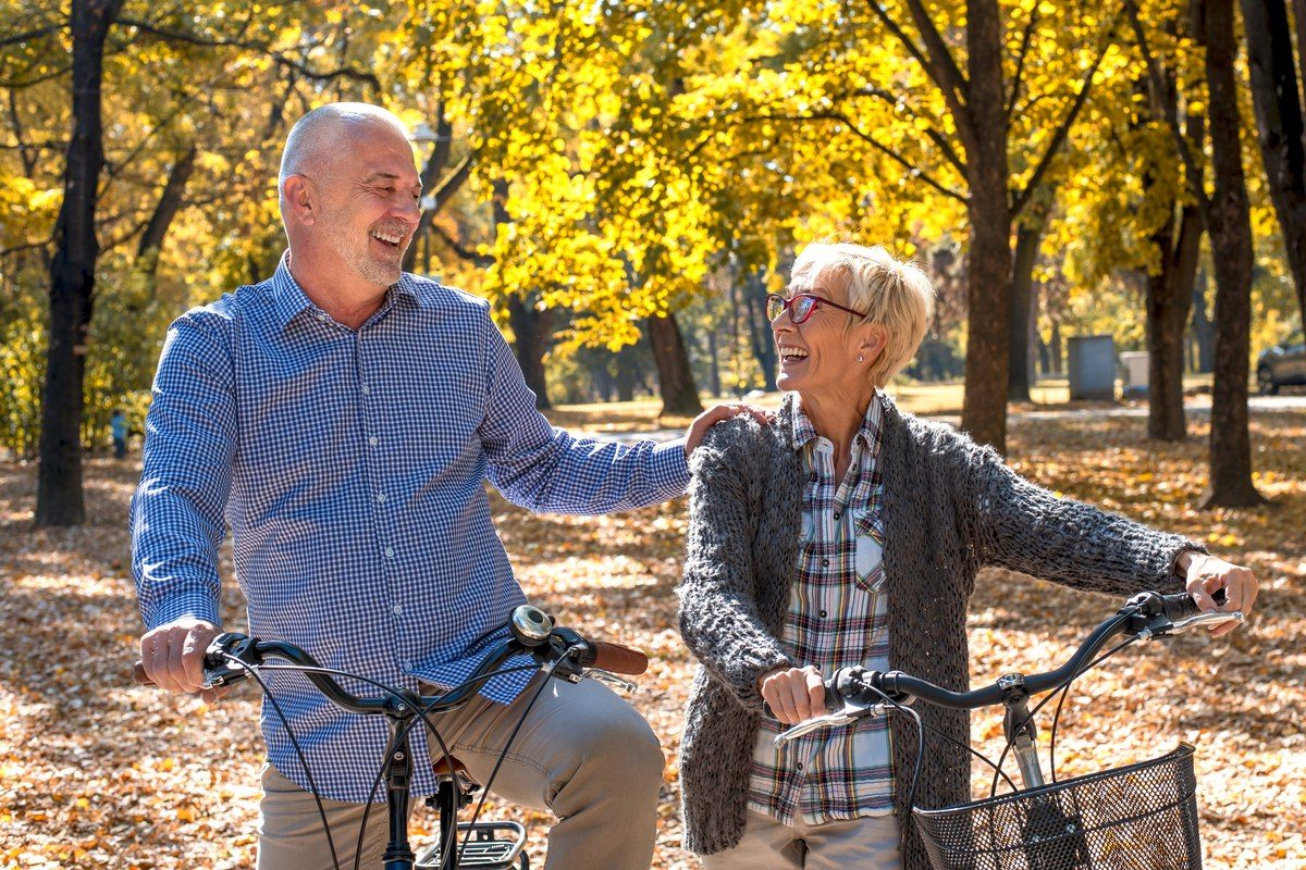 Een gepensioneerd koppel dat lachend samen fietst in een zonnig herfstpark