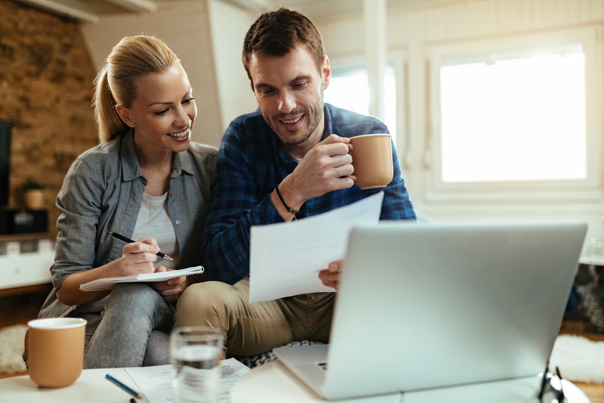 Een koppel dat glimlachend hun financiële papieren en laptop samen doorneemt met koffie