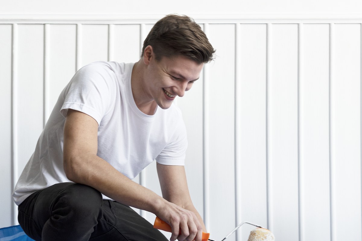 Een lachende man die met een verfroller een klus in huis aanpakt