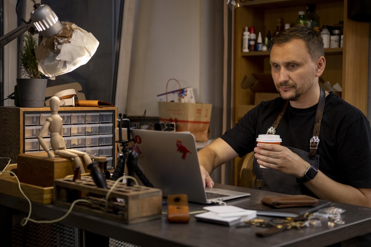 Een zelfstandige ondernemer aan zijn werkbank die zijn laptop raadpleegt tijdens een koffiepauze